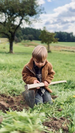 Kind spielt im Garten mit Schaufel auf grünem Rasen